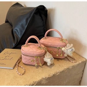 Pink quilted mini bag with gold chain strap and cute plush charm on a stone surface