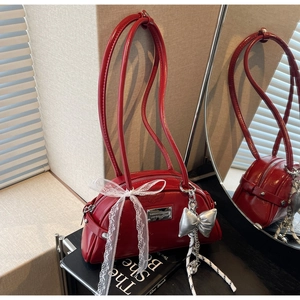 Détail d'un sac baguette en cuir verni rouge avec nœud en dentelle et plaque logo