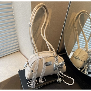 Détail d'un sac crème avec nœud en dentelle et pendentifs en forme de cœur argentés