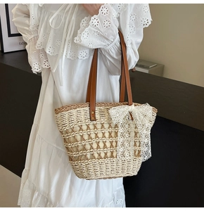 Détail d'un sac cabas en paille avec nœud en dentelle blanche et poignées en cuir marron