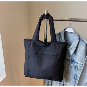 Detail of minimalist black tote bag with large front pocket and wide shoulder strap