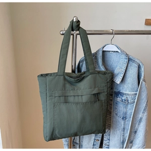 Detail of dark green quilted tote bag with front pocket showing soft padded nylon texture