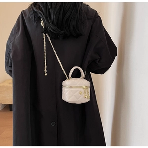 Close-up of cream quilted mini bag featuring gold chain strap and floral pendant on model