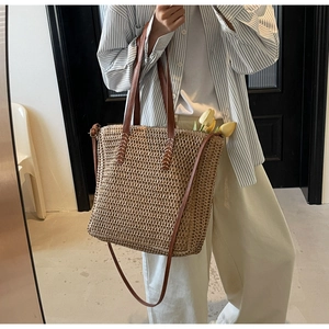 Détail d'un sac cabas en paille tissée avec poignées en cuir et touches florales