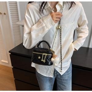 Detail of black quilted mini bag with gold chain strap and cute star charm on a model