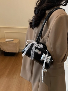 Sac à bandoulière en cuir verni noir avec nœud en dentelle blanche et pendentif argenté