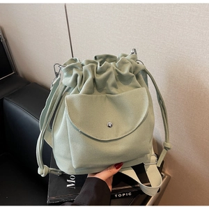 Dettaglio di una borsa a secchiello in tela verde chiaro con coulisse e tasca frontale