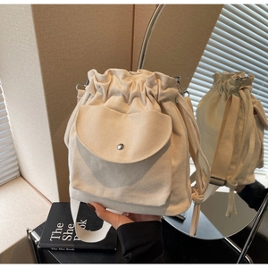 Dettaglio borsa a secchiello in tela beige con coulisse e tasca con fibbia metallica