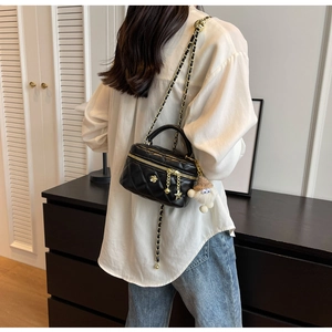 Detail of a black quilted mini bag featuring gold floral charms and a plush doll pendant