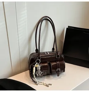 Dettaglio borsa in pelle verniciata marrone scuro con tasche e ciondolo a orso in metallo