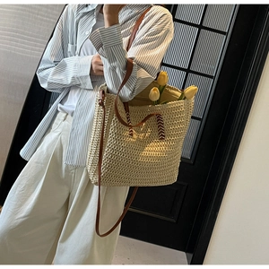 Détail du sac cabas en paille tissée avec poignées en cuir marron et coutures blanches décoratives