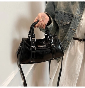 Detail of black glossy dumpling bag with silver hardware and adjustable strap on a model