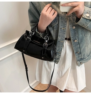 Detail of black patent leather dumpling bag with silver buckles and mirror-like finish