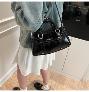 Detail shot of black glossy handbag with silver buckles and studs worn as a crossbody bag