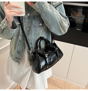 Detail of black glossy dumpling bag with pleated texture and silver metal buckles