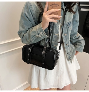 Model wearing a glossy black Boston bag with silver buckle straps and shoulder strap