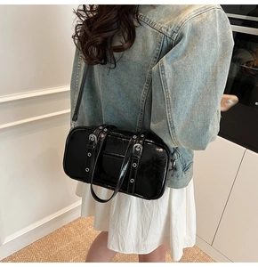 Detail of a shiny black patent leather Boston bag with silver hardware on a model