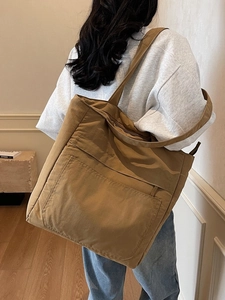 Large khaki canvas tote bag with front pocket shown as worn by a model in casual style