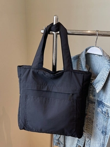 Black nylon tote bag with front zipper pocket shown in a lifestyle casual setting