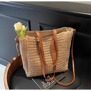 Détail d'un sac cabas en paille avec texture tissée, anses en cuir brun et doublure