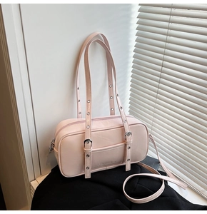 Detail of light pink faux leather shoulder bag with decorative metal eyelet straps and branding