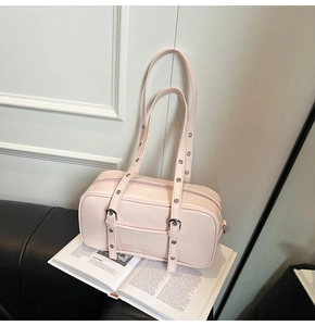 Pale pink leather Boston bag detail with silver eyelet straps on a black sofa