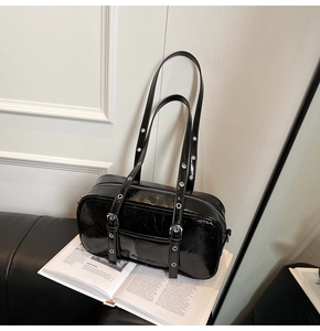 Detail of black glossy patent leather Boston bag with silver eyelet straps on magazine