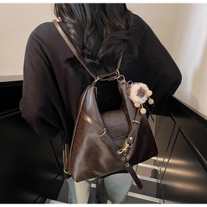 Detail of vintage brown leather tote bag with plush sheep charm worn as a backpack