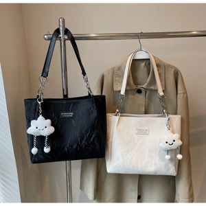 Detail of pleated tote bags with chain straps and plush charms on a khaki coat background