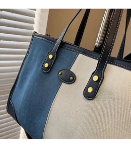 Detail of color-block tote bag featuring navy leather handles and gold rivet accents