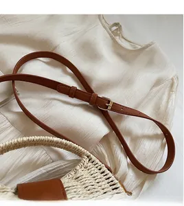 Detail of adjustable brown leather shoulder strap on a beige woven straw beach bag