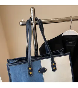 Detail of color-block denim tote bag showing leather straps and gold metal rivets