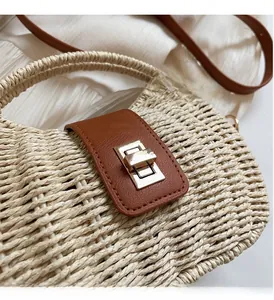 Detailaufnahme der beigen Strohtasche mit braunem Lederband und goldenem Metalldrehverschluss