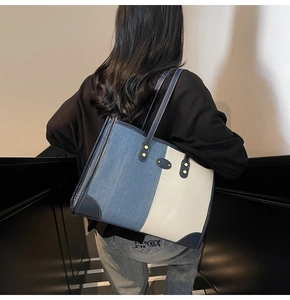 Denim tote bag with contrast stitching and metal studs shown on a model's shoulder