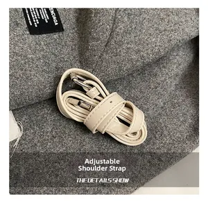 Détail d'une bandoulière réglable en cuir crème avec boucle argentée sur fond en laine grise