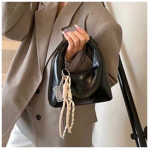 Détail du sac hobo en cuir verni noir avec charms décoratifs et gravure du logo