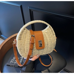 Close-up of woven straw bag detail featuring brown leather strap and silver twist lock
