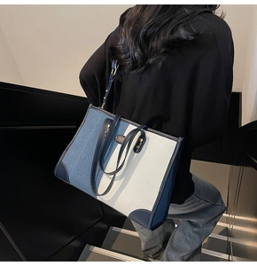 Detail of color-block tote bag featuring denim fabric, leather trim, and gold metal rivets
