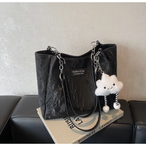 Detail of black tote bag with wrinkled PU texture, silver chains and cloud plush charm
