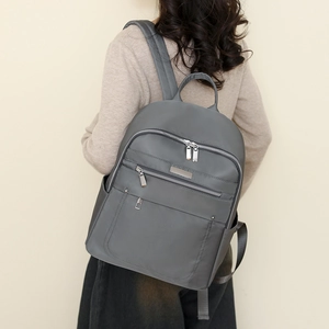 Rear view of model wearing a grey waterproof nylon backpack with multi-zipper pockets