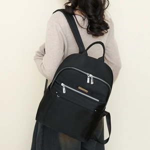 Rear view of model wearing a black waterproof nylon backpack with silver zipper details