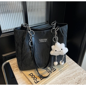 Detail of black textured tote bag with chain strap and white plush cloud charm