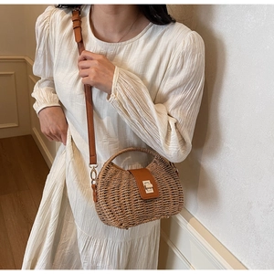 Close-up of a woven straw crossbody bag with brown leather flap and metal twist lock