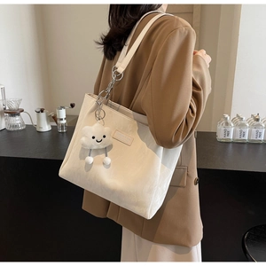 Detail of a large cream tote bag with a plush cloud charm and metal chain strap