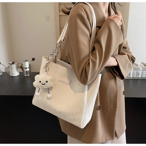 Detail of cream tote bag with cloud plush charm and chain strap in cafe setting