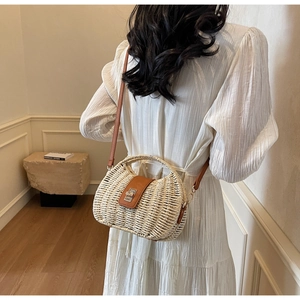 Detail of woven straw bag with leather strap and metal twist lock on model