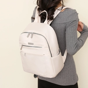 Rear view of a minimalist cream white nylon backpack worn by a model for daily use