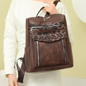 Detail of leopard print stitching and multi-zipper pockets on brown leather backpack