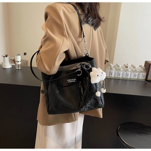 Detail of black pleated tote bag with metal chain strap and white plush cloud charm