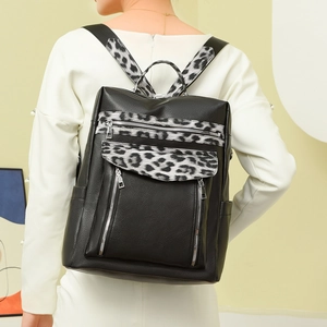 Detail view of black faux leather backpack with leopard print straps on a model